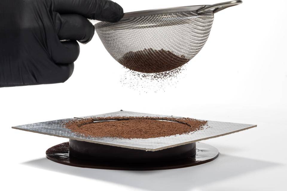 chef polvilhando pó de cacau em cima de entremet