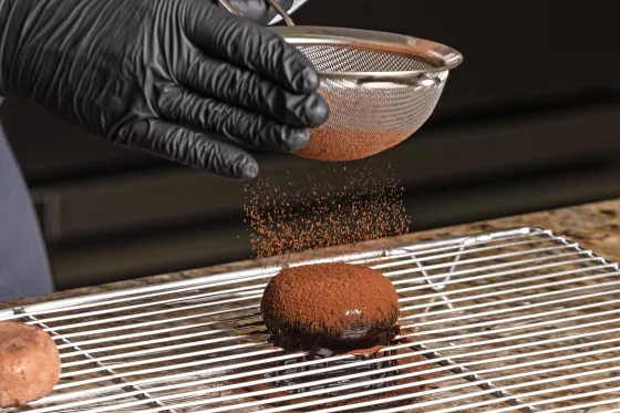 chef polvilhando pó de cacau em cima de entremet